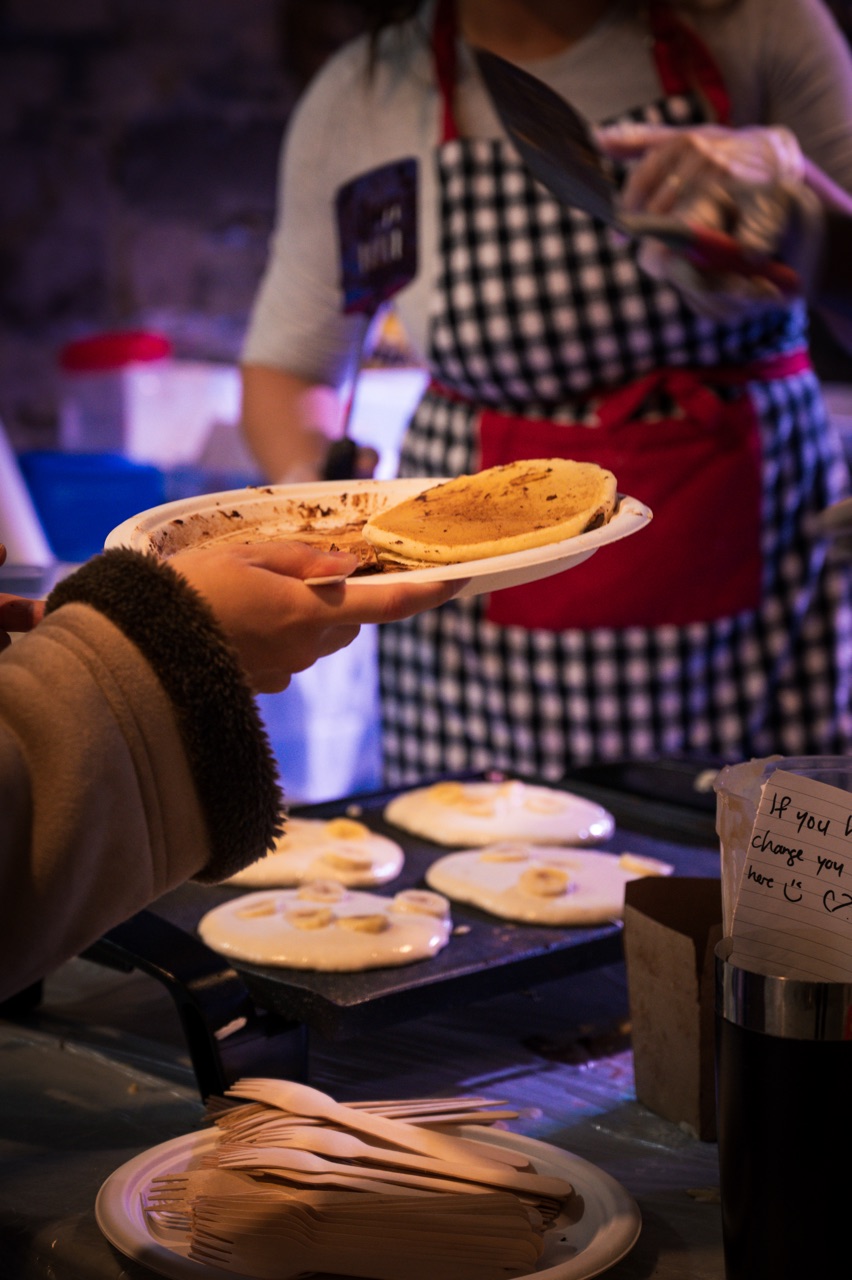 Volunteer handing off a paper plate of free pancakes at the Pancakes & Booze show